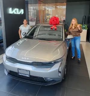 Un KIA gris con moño rojo y dos asesoras