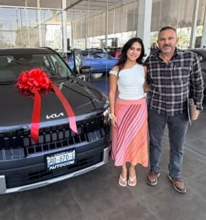 Una pareja con su KIA negro decorado con un moño rojo